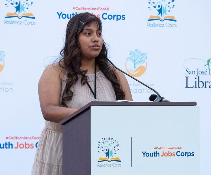 A speaker at Resilience Corps 2023 Graduation at a podium that reads 'Youth Jobs Corps'.