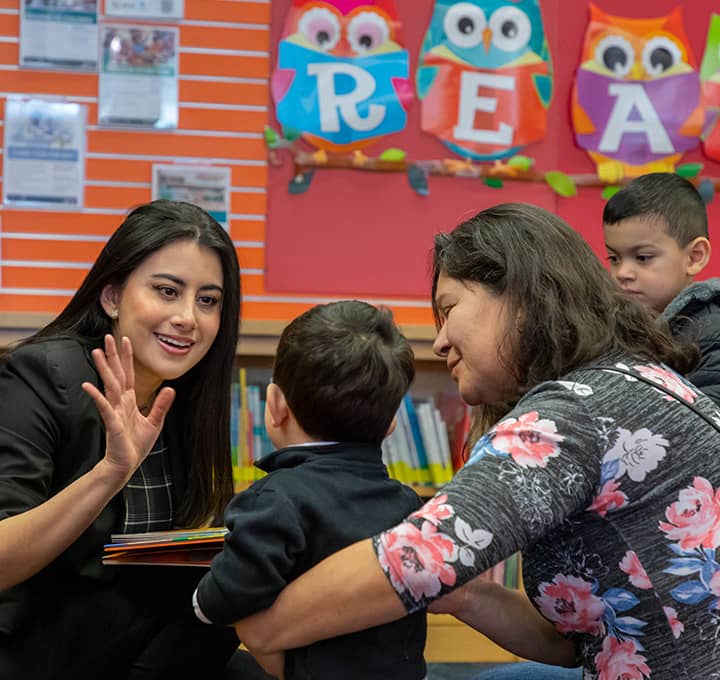 Woman greeting a child in a library classroom.