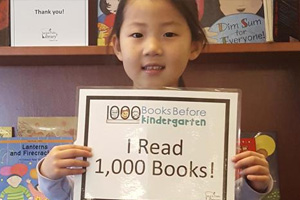 Young girl holding up a 1,000 book reading achievement certificate.