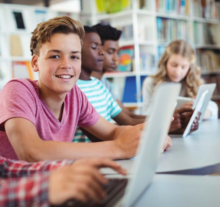 A kid looking up and smiling from his computer while working in a small group.