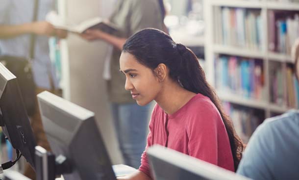 A woman focused at a desktop computer in the library.