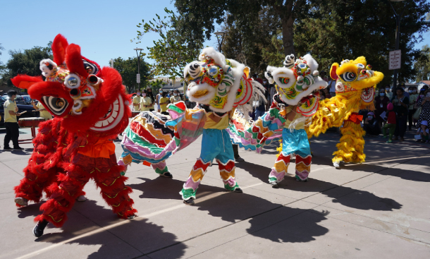 Four traditional Chinese lions dance outdoors while spectators watch.