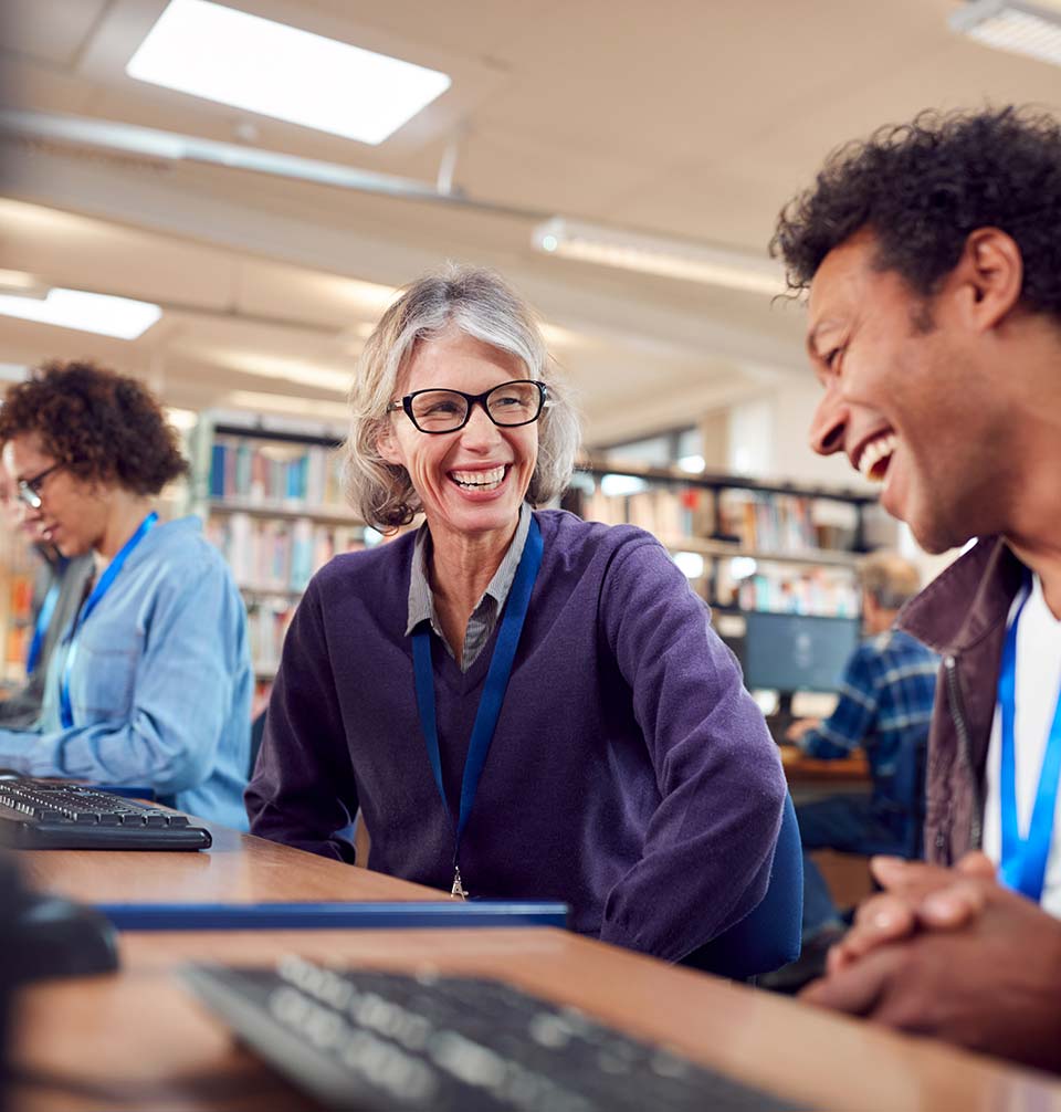 A man and woman laughing while working at the library's computer desk.