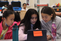 Three girls examine an iPad.