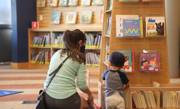 A mother and child look through children's books in the library.